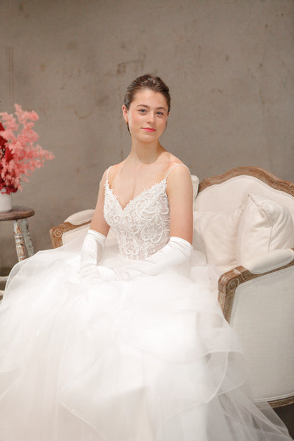 Woman in a white wedding dress sitting on a decorative chair with a floral arrangement in the background.