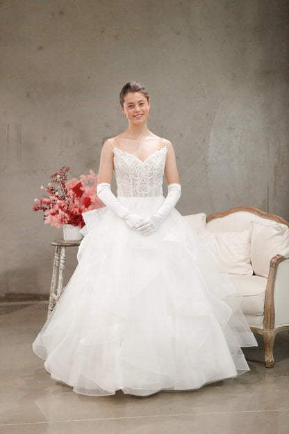 Woman in a white wedding dress standing in a room with a floral arrangement and a couch.