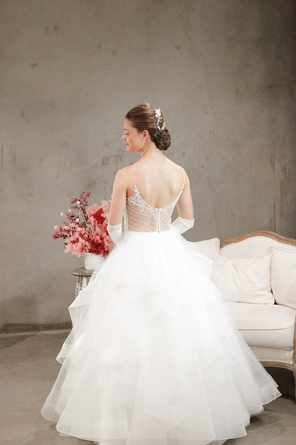Woman in a white wedding dress holding flowers in a room with a gray wall and white couch.
