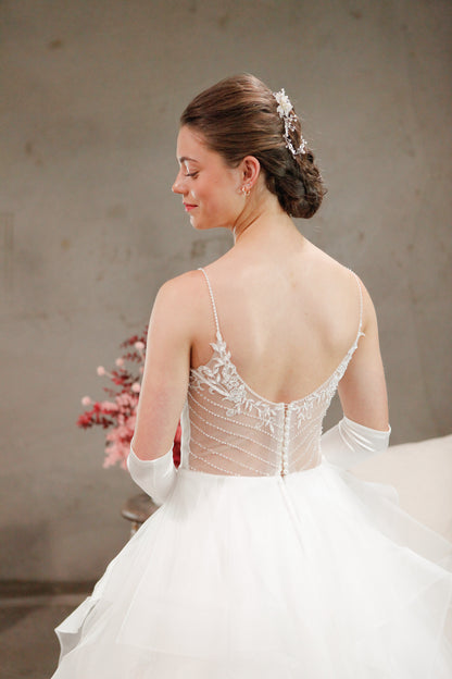 Woman in a white wedding dress with a lace back and floral hairpiece, sitting against a neutral background.