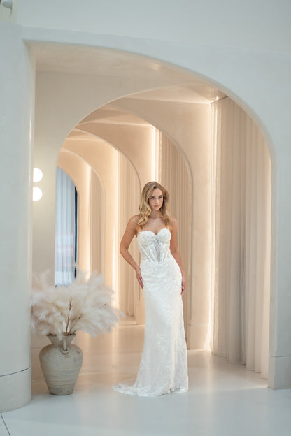Woman in a strapless white wedding dress standing in a modern architectural setting with arches and soft lighting.