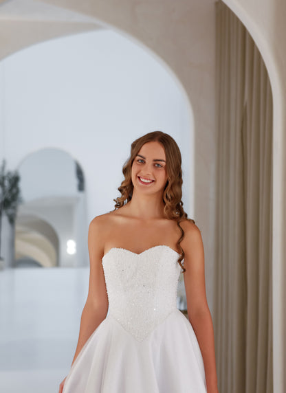 Woman in a white strapless dress standing in an elegant indoor setting.