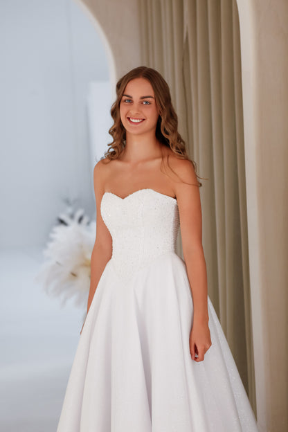 Woman in a strapless white wedding dress standing against a neutral background