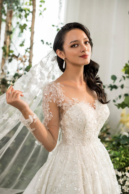 Woman in a white wedding dress with lace details, standing outdoors with greenery in the background