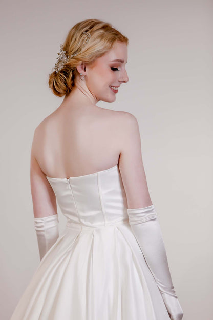 Woman in a white strapless gown with long gloves, standing against a plain background