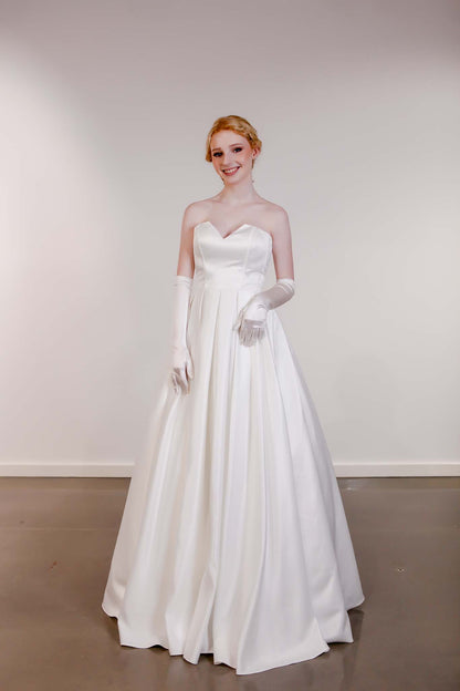 Woman in a white strapless gown with gloves standing against a plain background