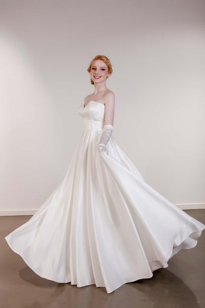 Woman in a white wedding dress with gloves against a plain background