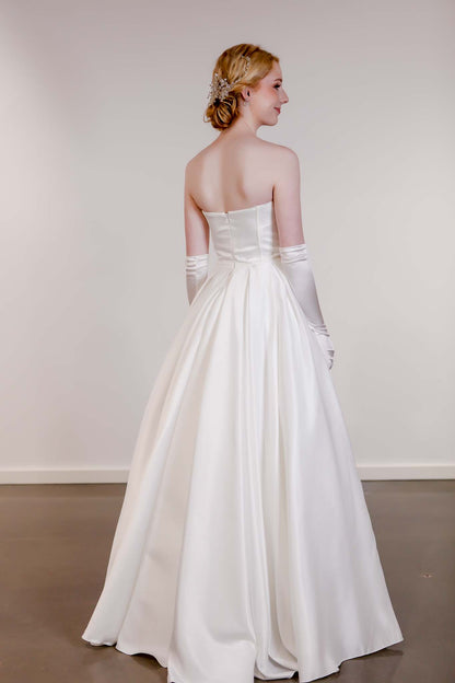 Woman in a white wedding dress with gloves standing against a plain background