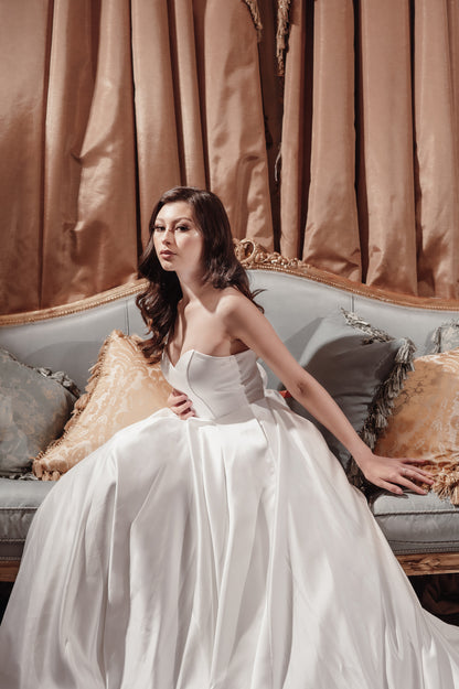 Woman in a white dress sitting on a decorative couch with gold curtains in the background