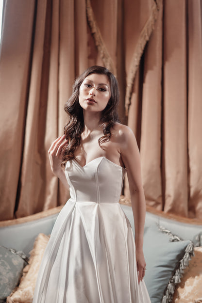 Woman in a white strapless dress standing in front of a draped curtain.