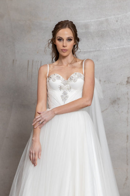 Woman wearing a white wedding dress with a cape against a gray background