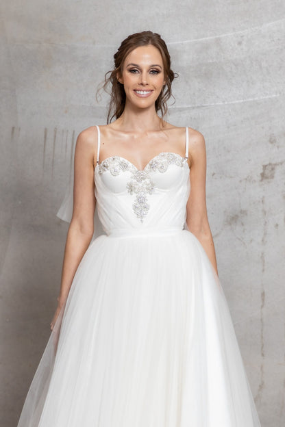 Woman wearing a white wedding dress with floral embellishments against a gray background