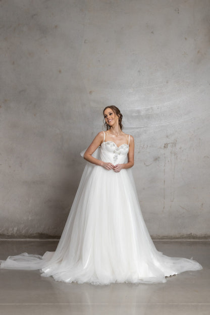 Woman in a white wedding dress standing against a plain wall.