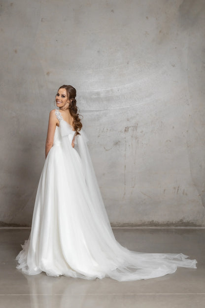 Woman in a white wedding dress standing against a plain wall.