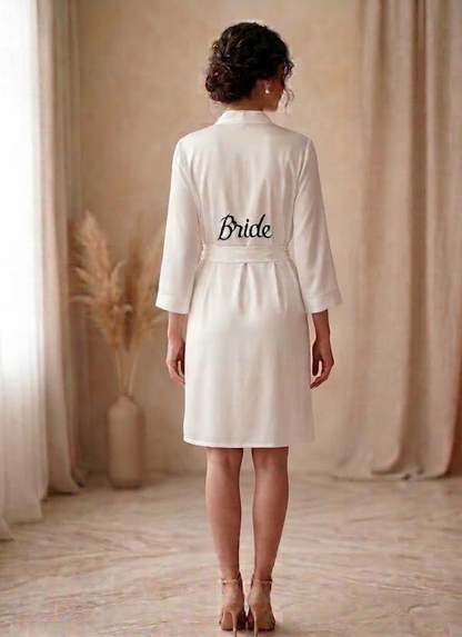 Person wearing a white robe with 'Bride' printed on the back, standing in a softly lit room.