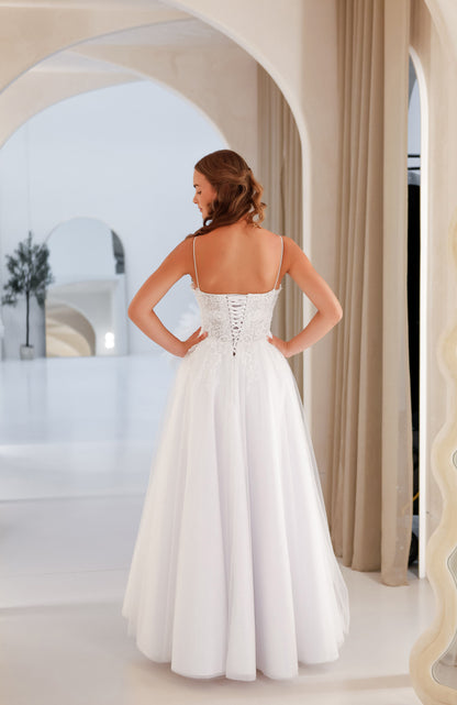 Woman in a white wedding dress standing in a bright, open space with architectural elements.