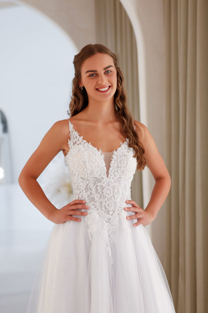 Woman wearing a white wedding dress with lace detailing in an indoor setting.