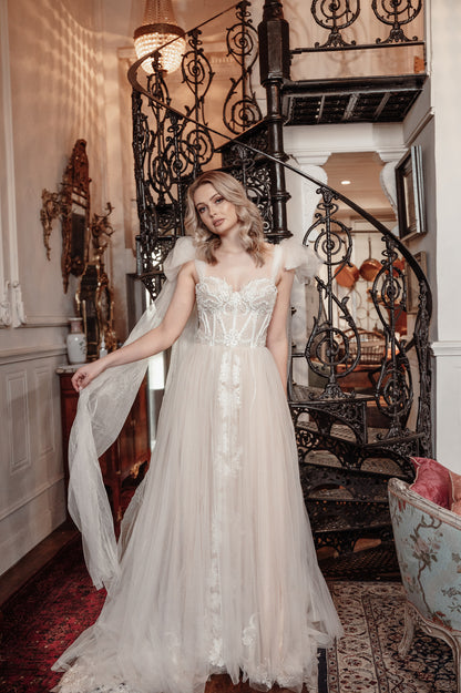 Woman in a white wedding dress standing in an elegant interior setting with a staircase
