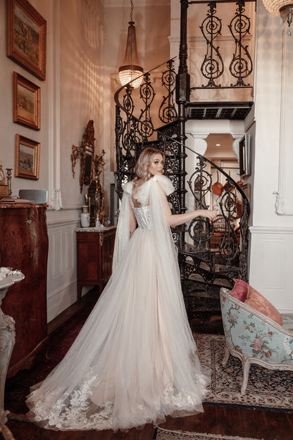 Woman in a white wedding dress standing in an elegant interior setting with a staircase