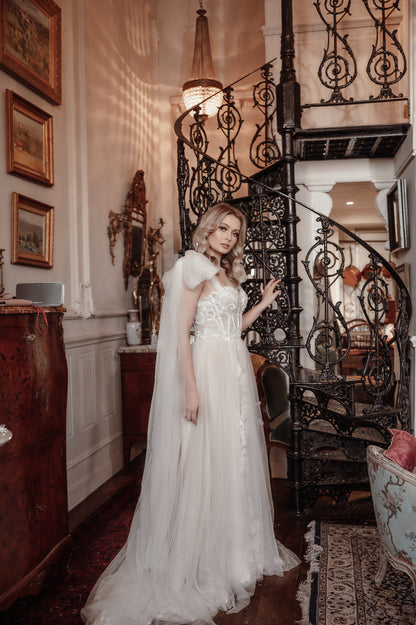 Woman in a white dress standing in an elegant interior setting with a staircase