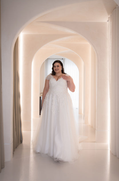 Woman in a white wedding dress standing in a row of arches with soft lighting.