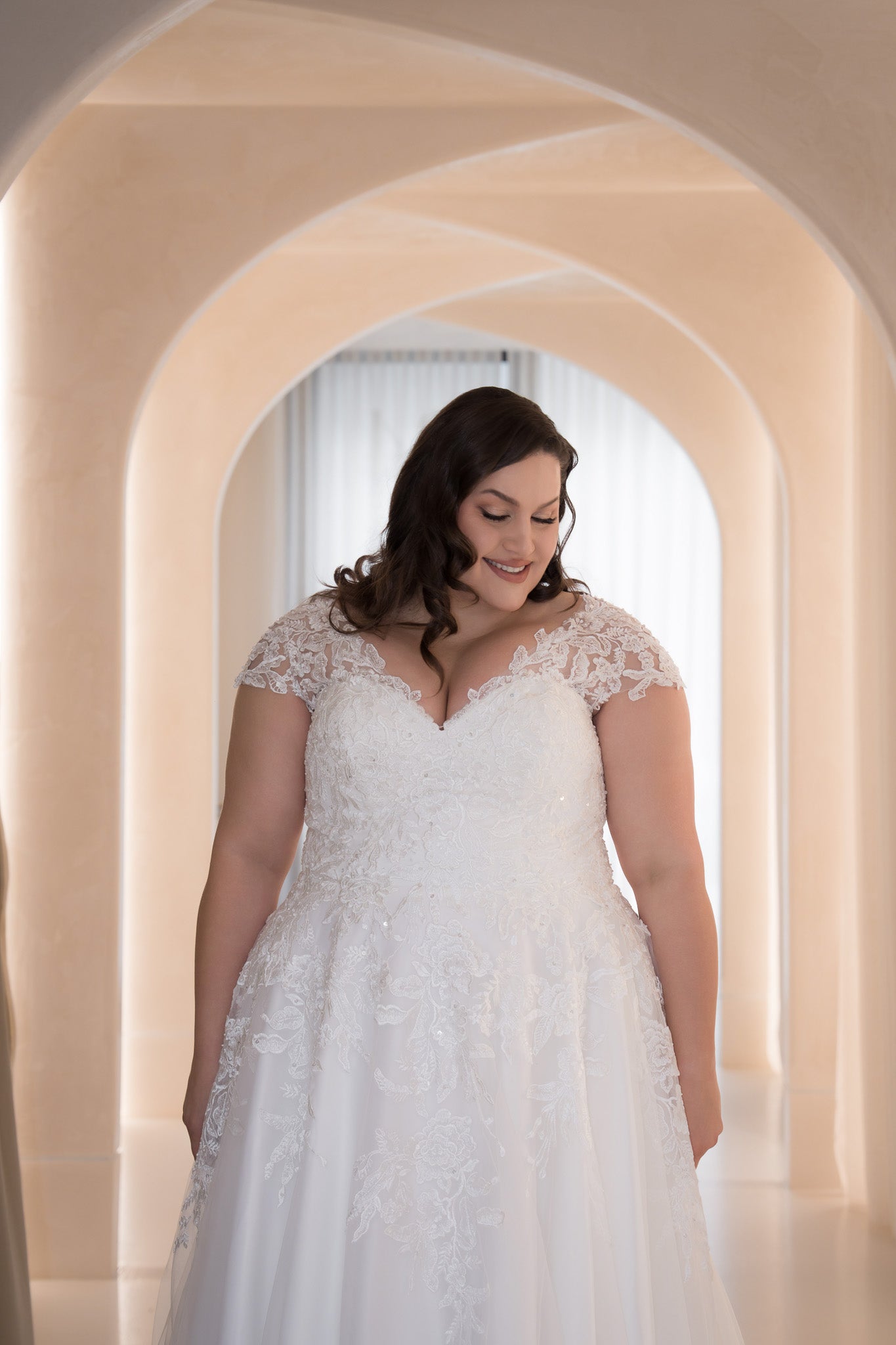 Woman in a white lace wedding dress standing in an archway.