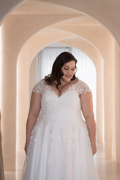 Woman in a white lace wedding dress standing in an archway.