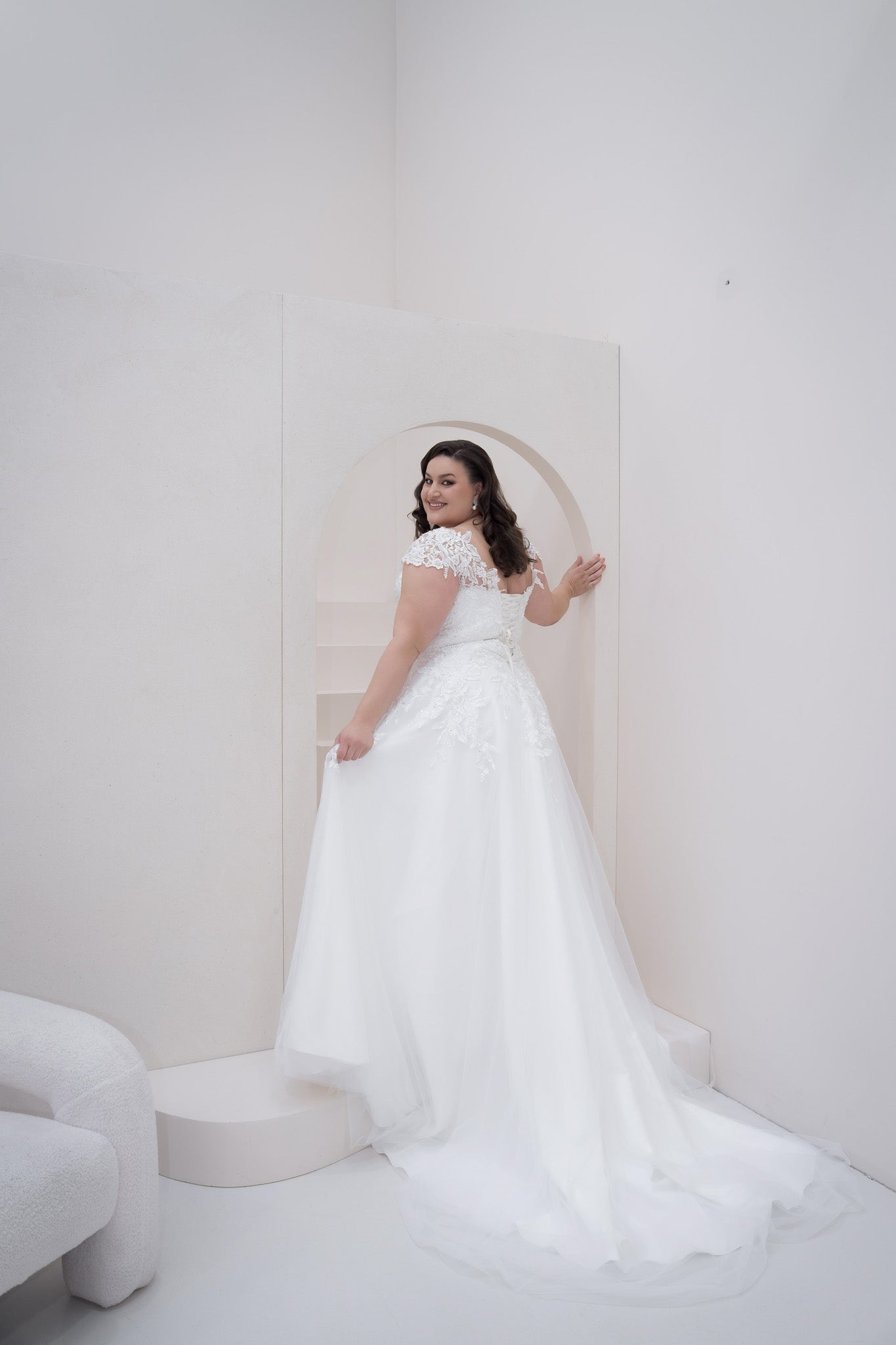 Woman in a white wedding dress standing in a minimalistic room with a white background