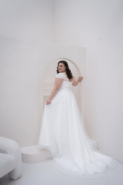Woman in a white wedding dress standing in a minimalistic room with a white background