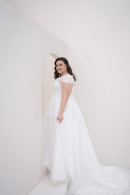 Woman in a white wedding dress posing against a plain background