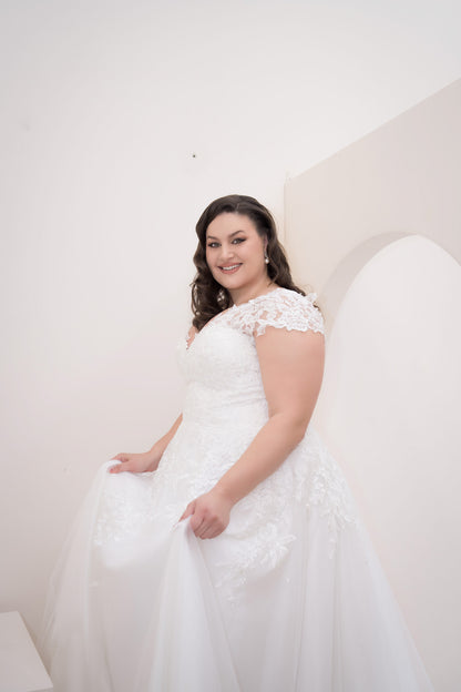 Woman wearing a white wedding dress with lace details against a plain background