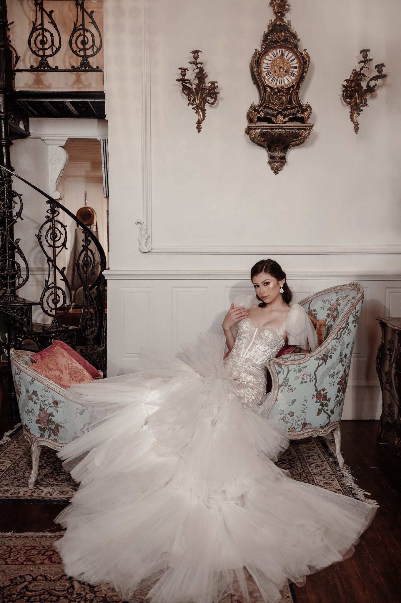 Woman in a white wedding dress sitting on an ornate chair in a grand room with decorative elements.
