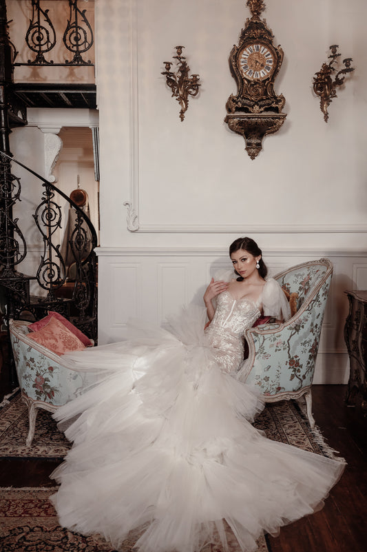 Woman in a white wedding dress sitting on an ornate chair in a grand room with decorative elements.