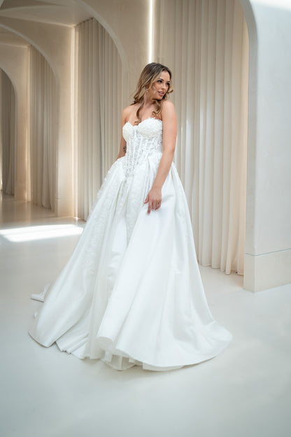 Woman in a white strapless gown standing in a bright, minimalistic room with arches.