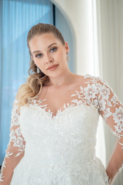 Woman wearing a white wedding dress with lace sleeves indoors.