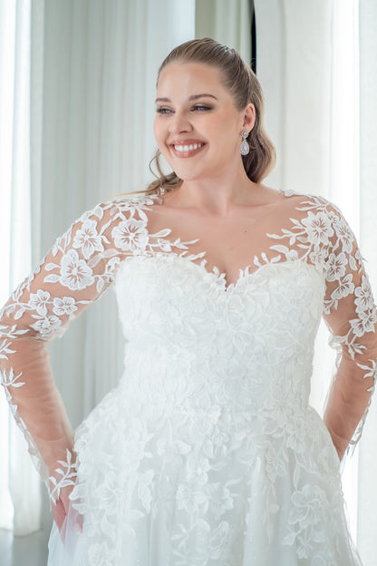 Woman wearing a white lace wedding dress indoors with curtains in the background