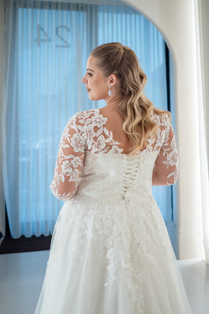 Woman wearing a white lace wedding dress with long sleeves in a softly lit room.