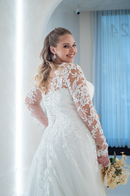 Woman in a white wedding dress with lace sleeves standing indoors.