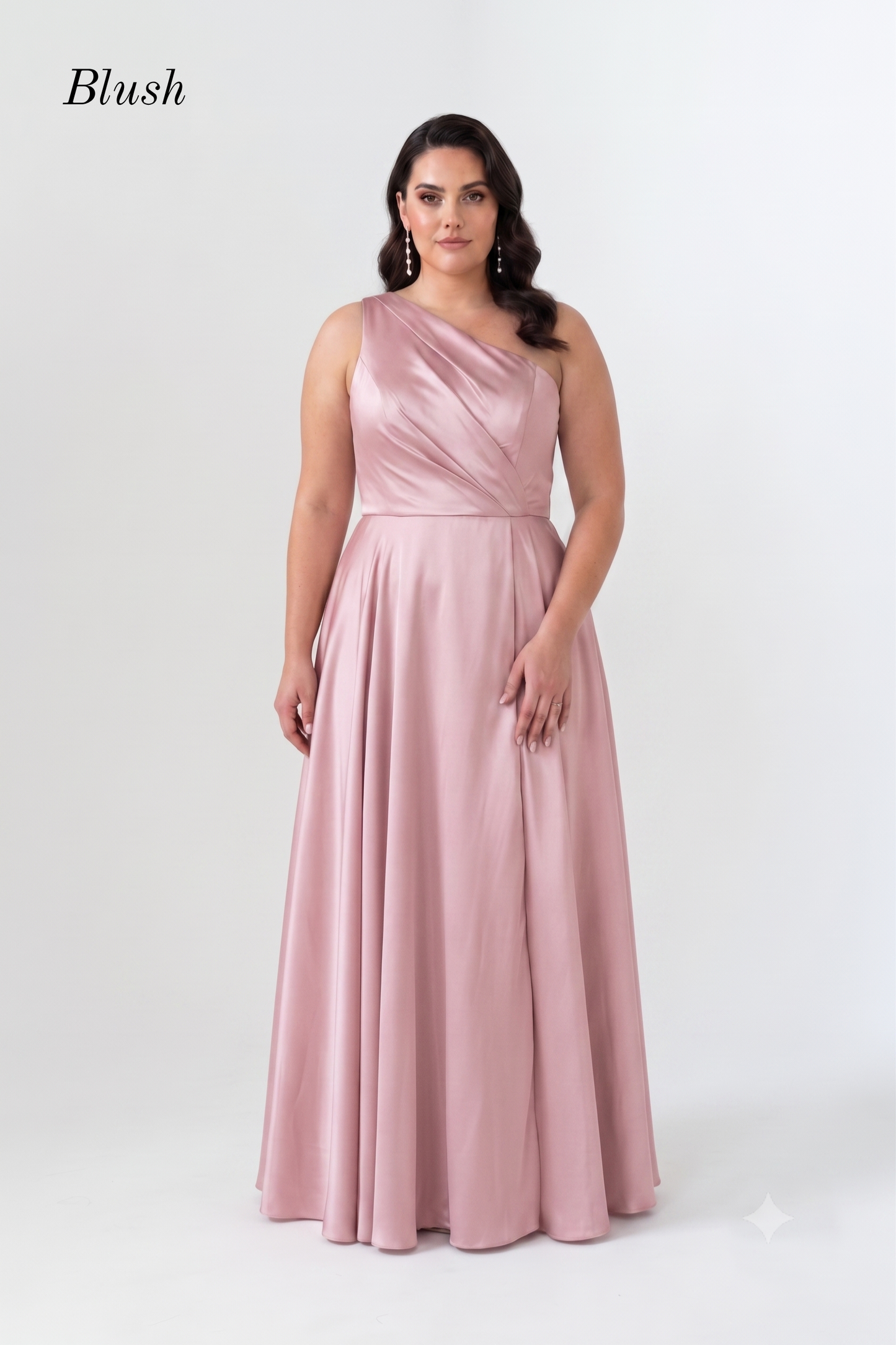 A woman modeling a blush pink, one-shoulder floor-length gown with a satin-like finish, set against a plain light gray studio background. The brand name 'Blush' is printed in the upper left corner.