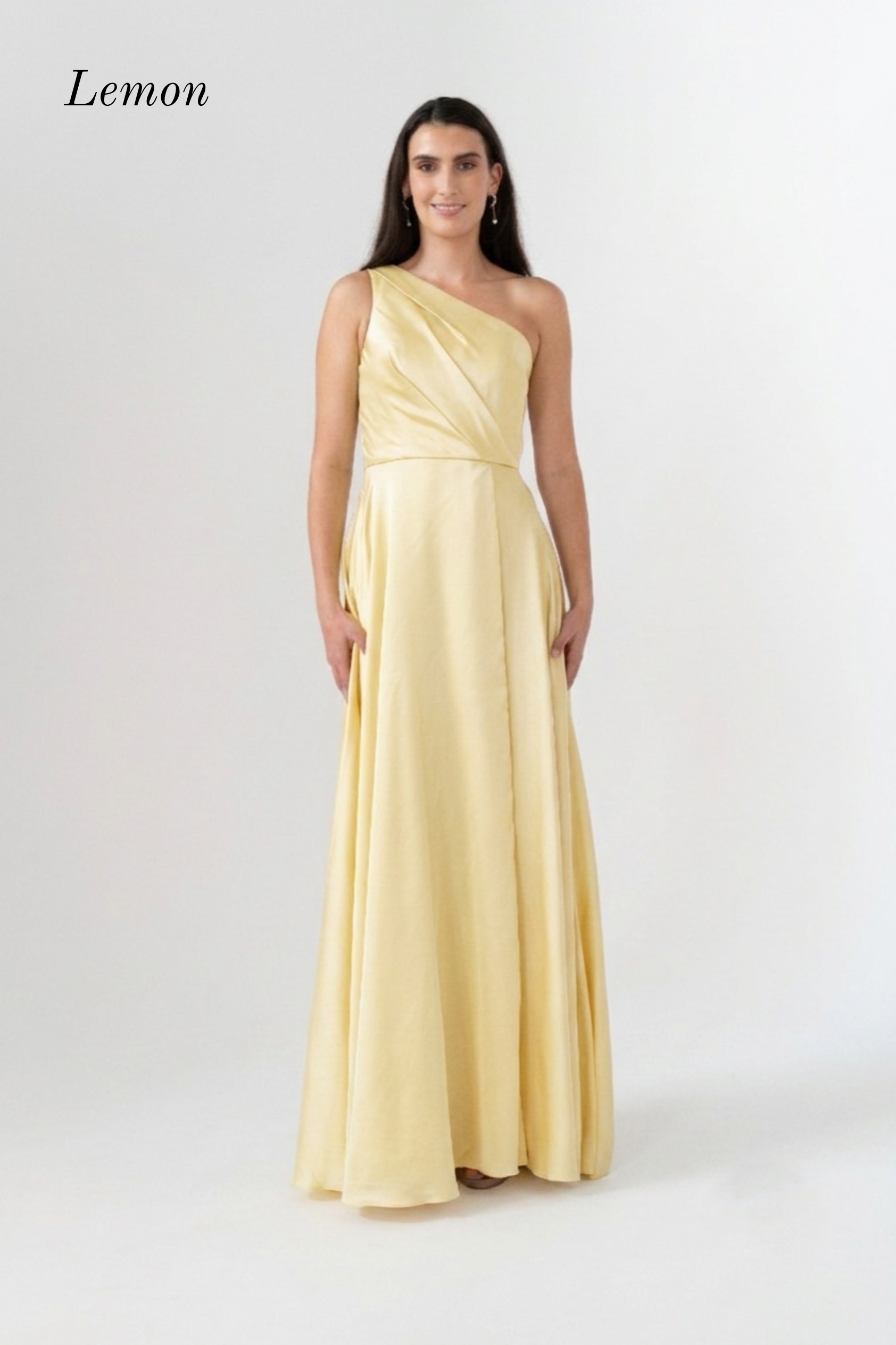 A woman modeling a floor-length one-shoulder gown in a pale lemon satin fabric against a plain light gray studio background. The word 'Lemon' appears in the upper left corner.