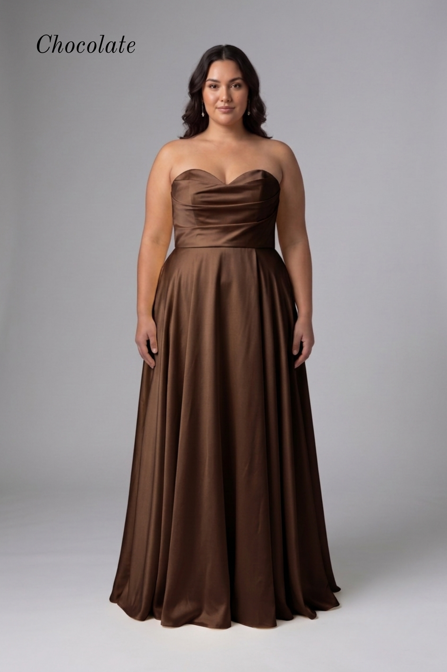 A woman modeling a floor-length chocolate brown strapless gown with a sweetheart neckline, ruched bodice, and flowing skirt against a light gray studio background. The word 'Chocolate' appears in the upper left.