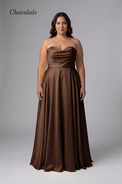 A woman modeling a floor-length chocolate brown strapless gown with a sweetheart neckline, ruched bodice, and flowing skirt against a light gray studio background. The word 'Chocolate' appears in the upper left.
