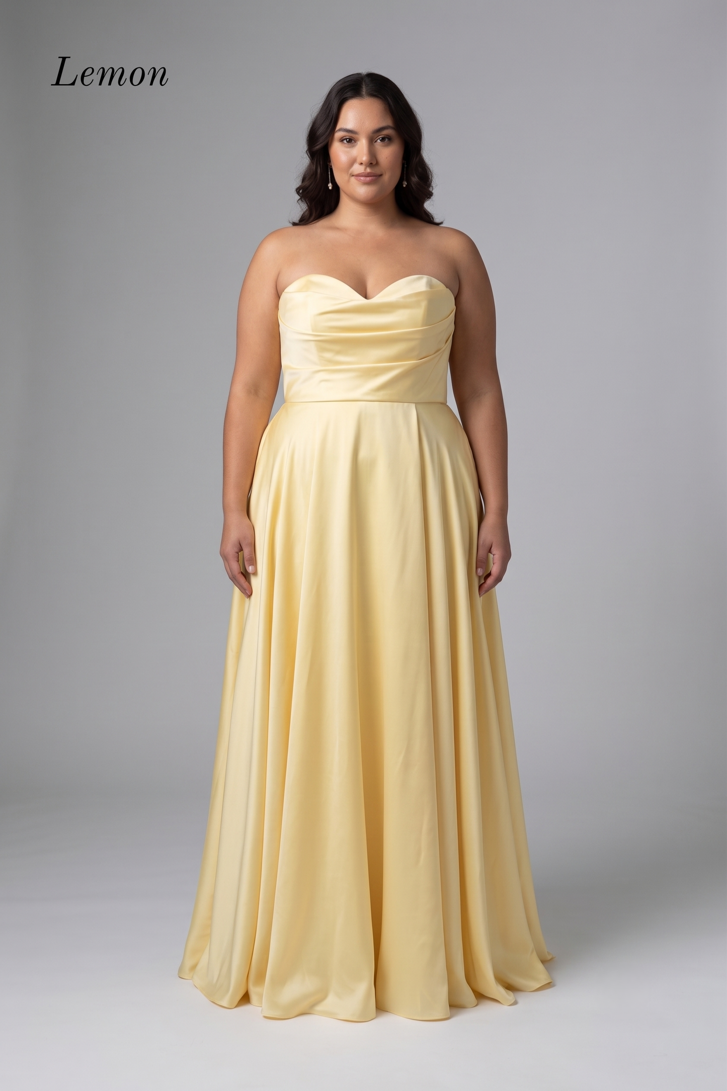 A woman modeling a strapless lemon yellow floor-length gown with a sweetheart neckline, ruched bodice, and flowing skirt against a light gray studio background. The word 'Lemon' appears in the upper left corner.