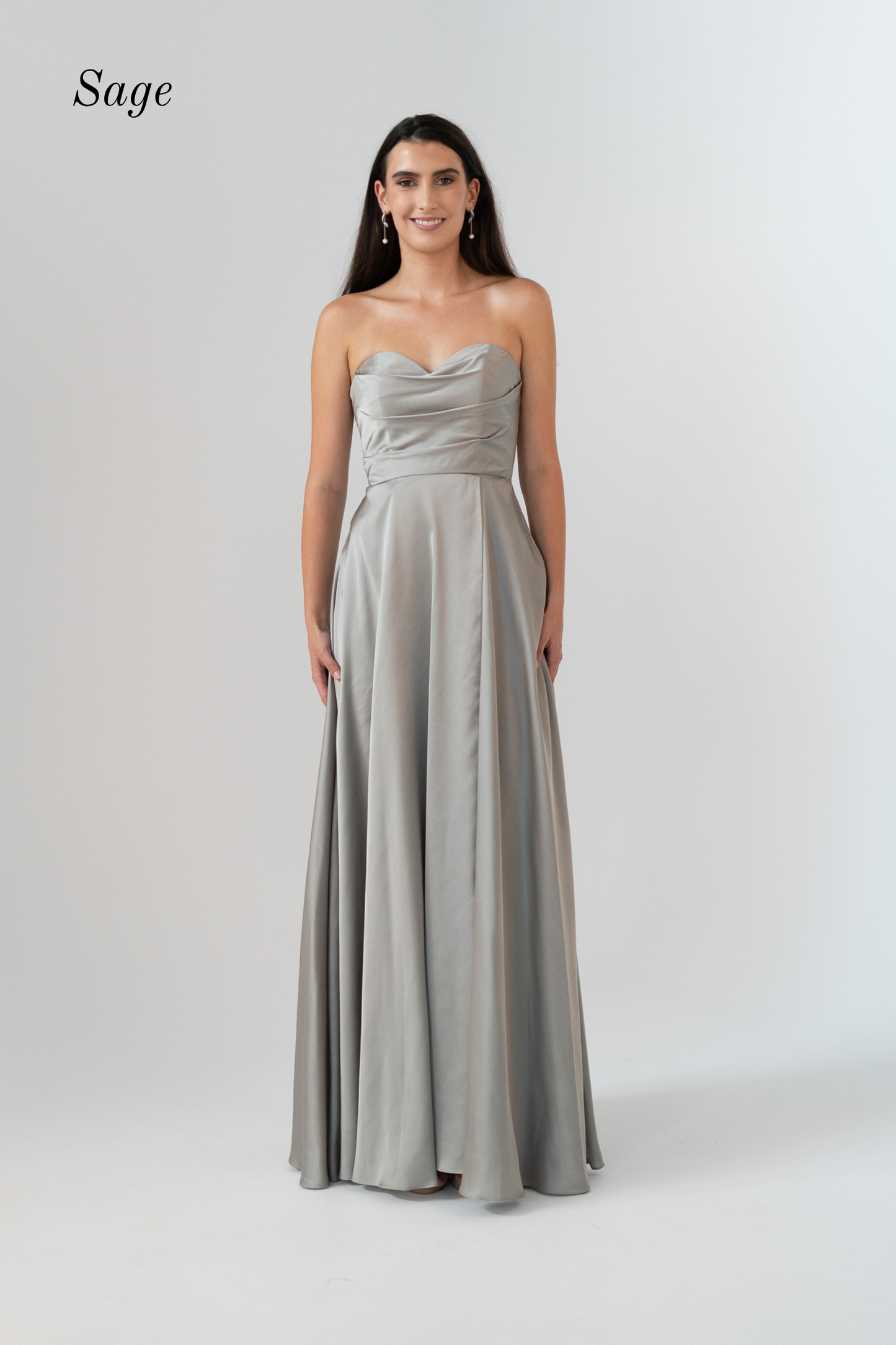 A woman modeling a floor-length sage green strapless gown with a ruched bodice and flowing skirt, standing against a light gray studio background. The word 'Sage' appears in the upper left corner.