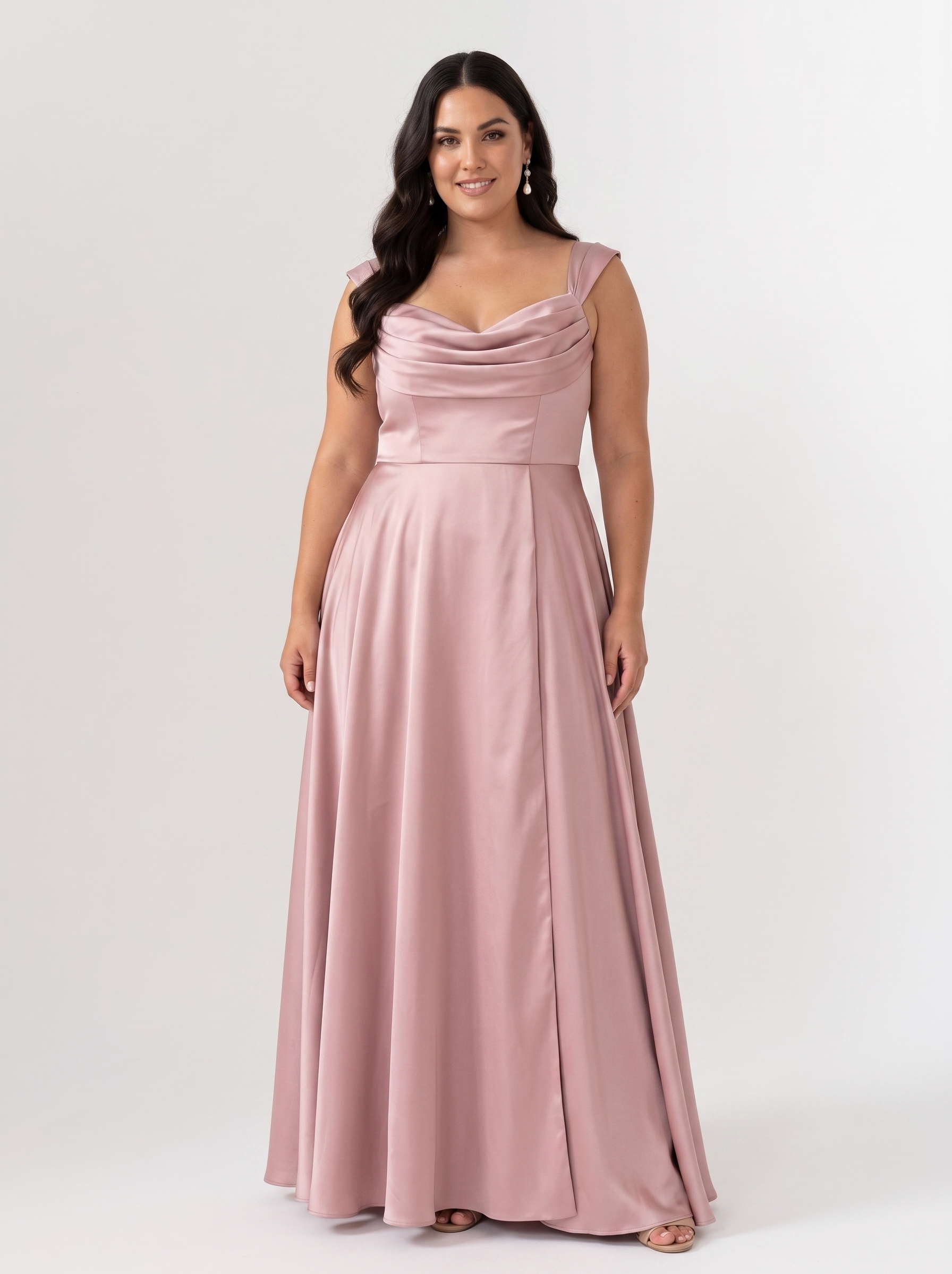 A woman modeling a floor-length dusty pink satin gown with a draped sweetheart neckline and a fitted waist, photographed against a plain light gray studio background.