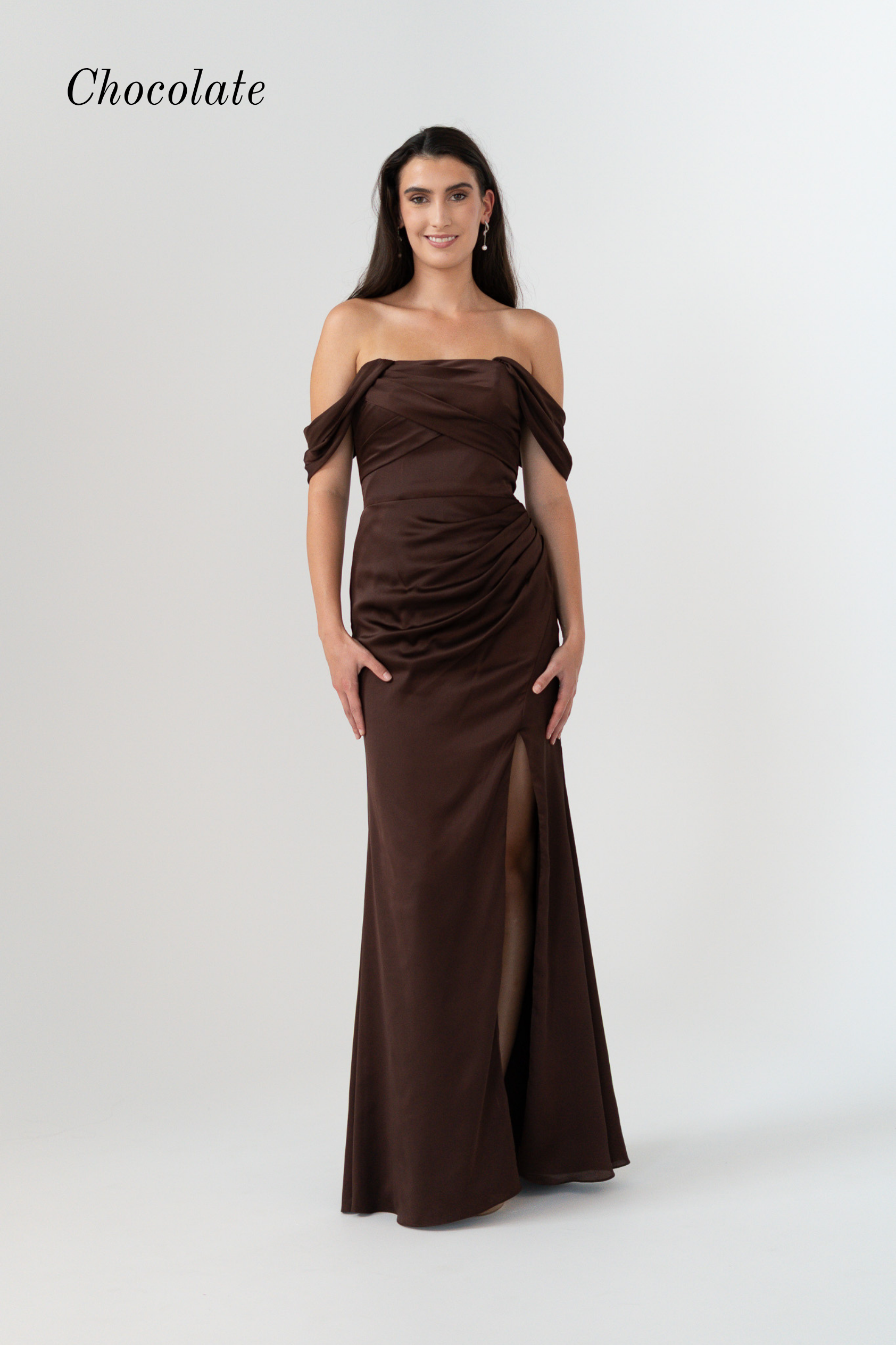 A woman modeling an off-the-shoulder chocolate brown floor-length gown with a ruched bodice and thigh-high slit, shown against a light gray studio background with the word 'Chocolate' in the top left.
