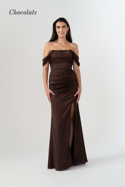 A woman modeling an off-the-shoulder chocolate brown floor-length gown with a ruched bodice and thigh-high slit, shown against a light gray studio background with the word 'Chocolate' in the top left.