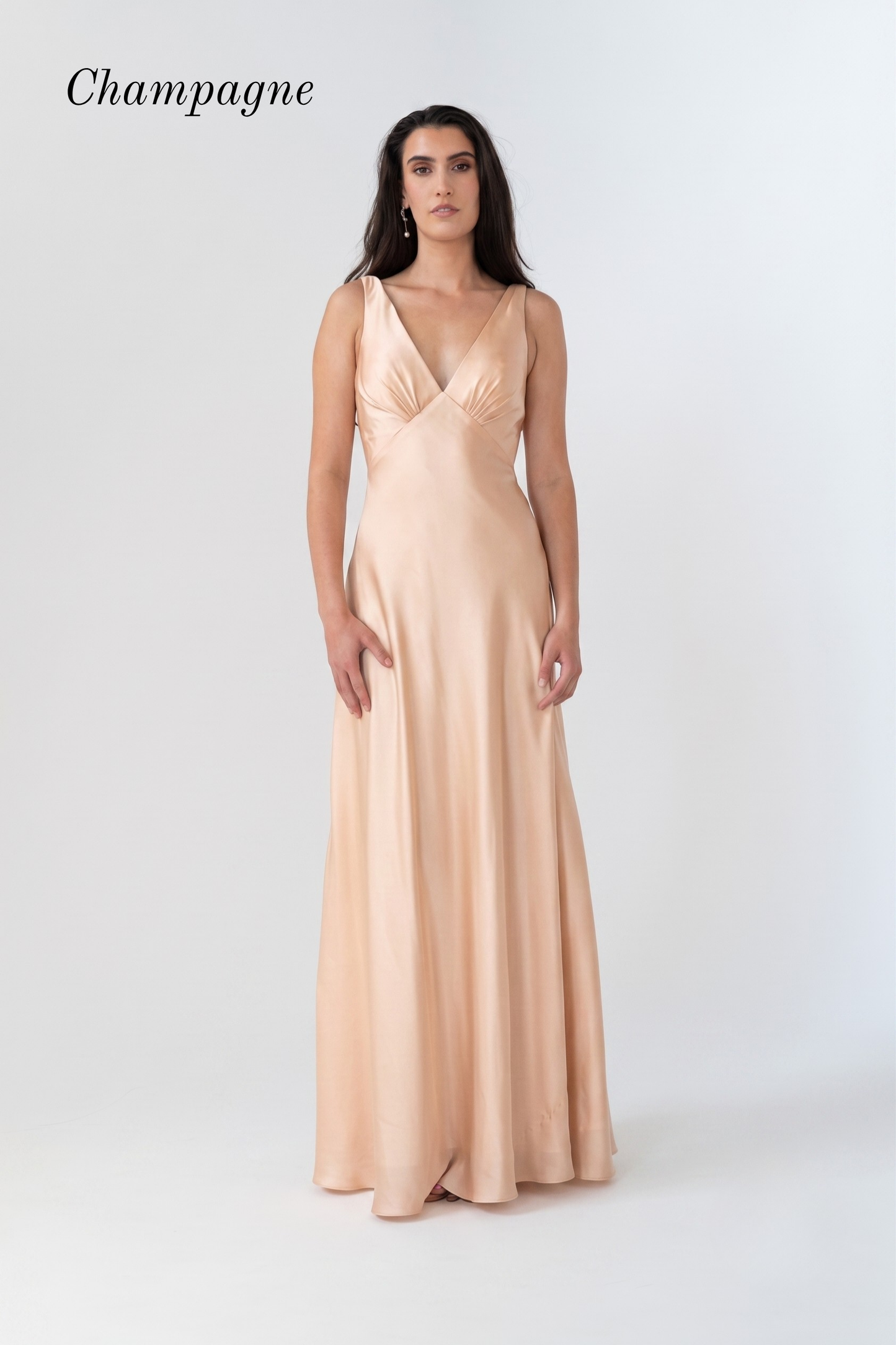 A woman modeling a floor-length champagne satin gown with a V-neckline and sleeveless design, set against a plain light gray studio background with the word 'Champagne' in the top left.