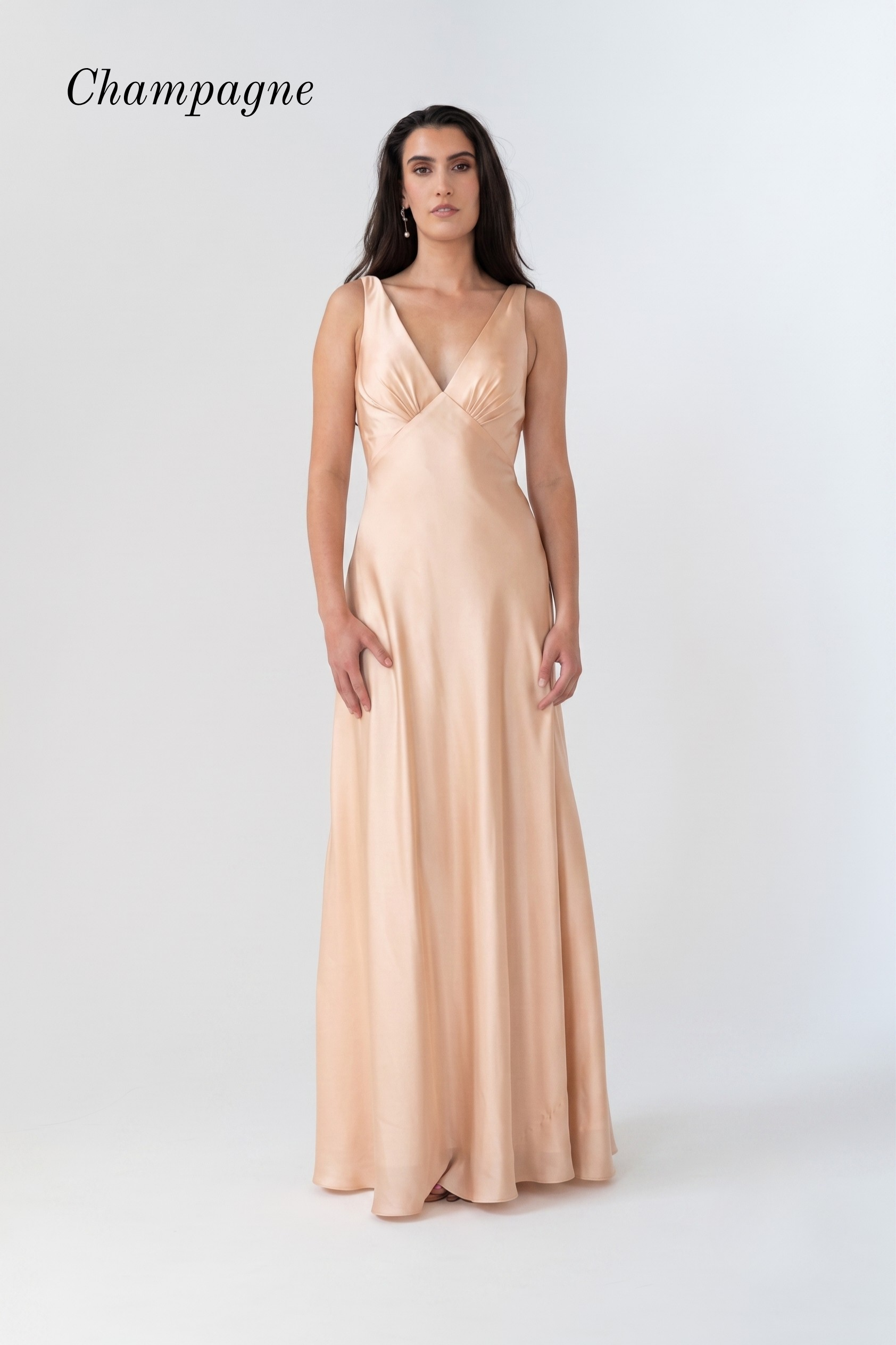 A woman modeling a floor-length champagne satin gown with a V-neckline and sleeveless design, set against a plain light gray studio background with the word 'Champagne' in the top left.