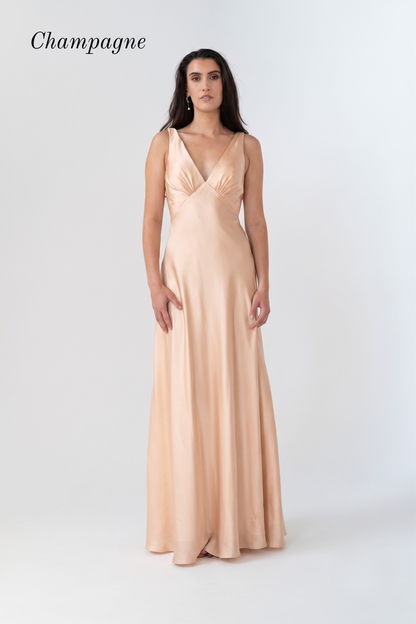 A woman modeling a floor-length champagne satin gown with a V-neckline and sleeveless design, set against a plain light gray studio background with the word 'Champagne' in the top left.